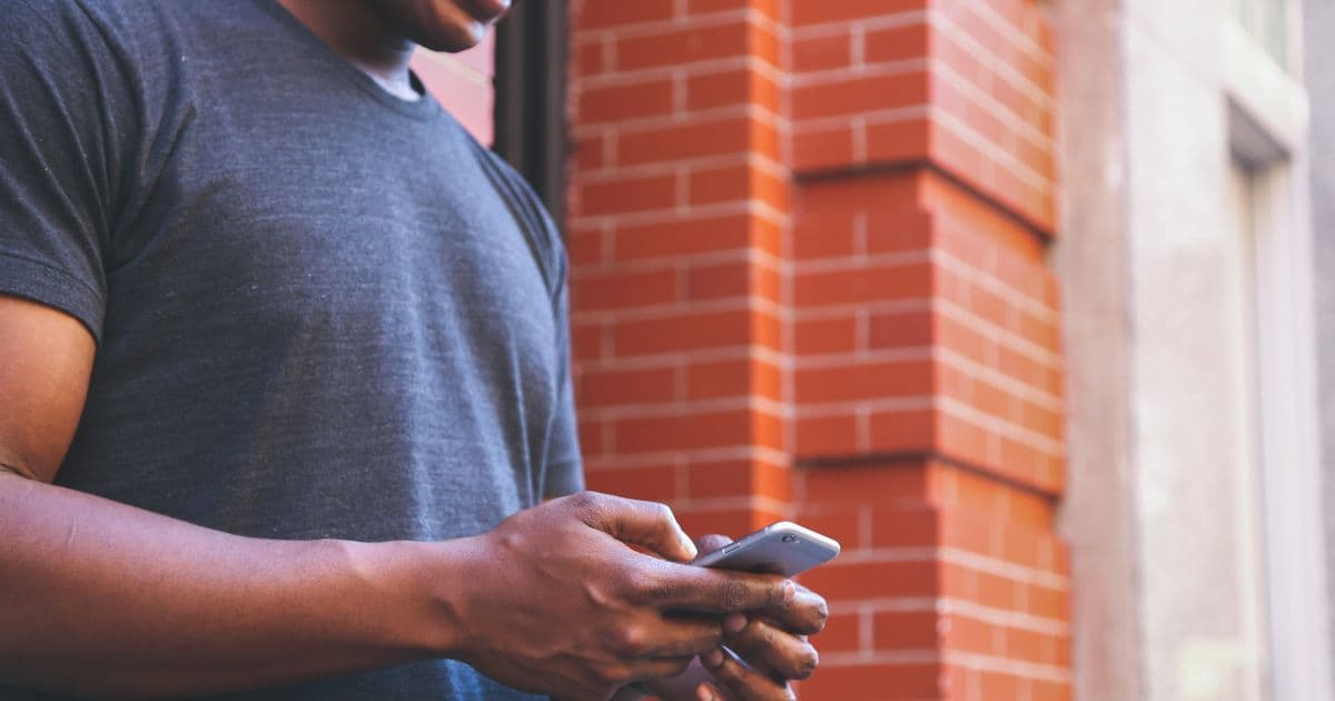 Person tippt eine Nachricht auf dem Smartphone, im Hintergrund eine Backsteinfassade