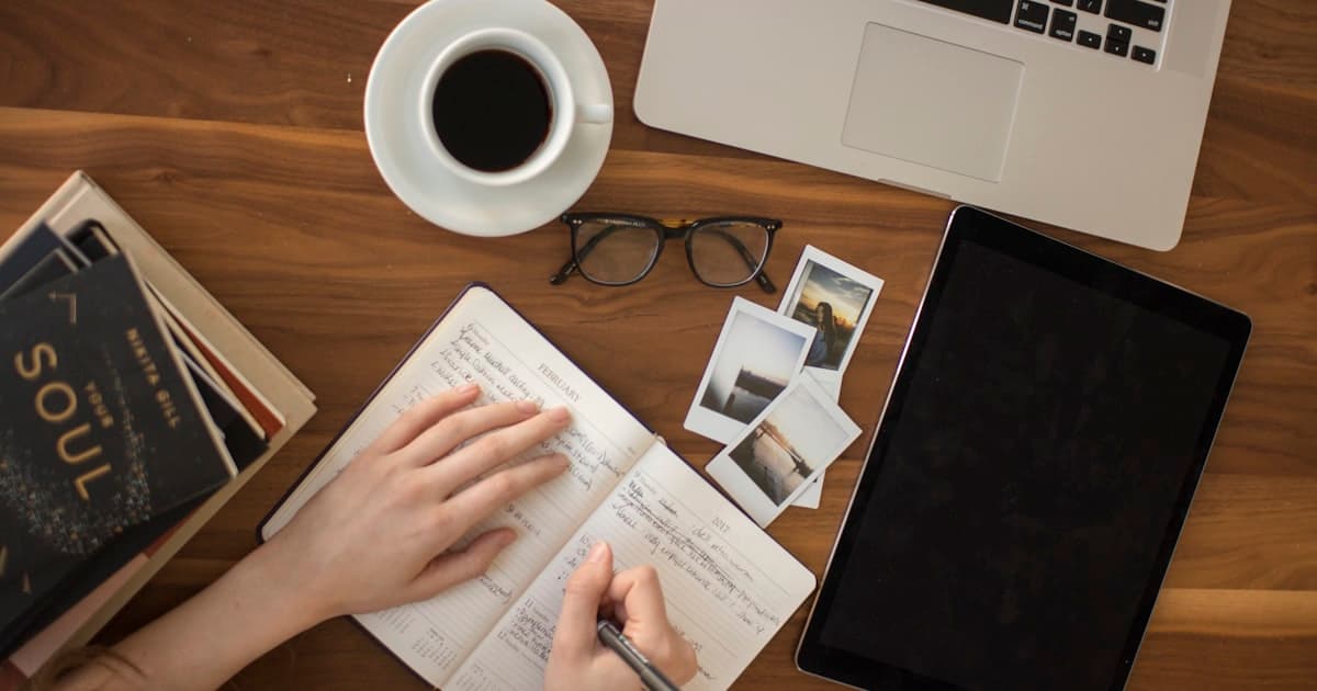 Arbeitsplatz mit Notizbuch, Laptop und Brille in einem kleinen Büro