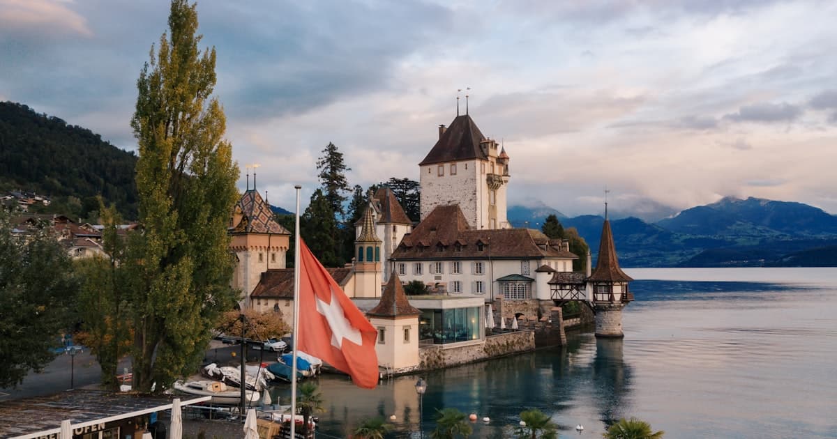 Schloss Oberhofen am Thunersee mit Schweizer Flagge und Bergen im Hintergrund