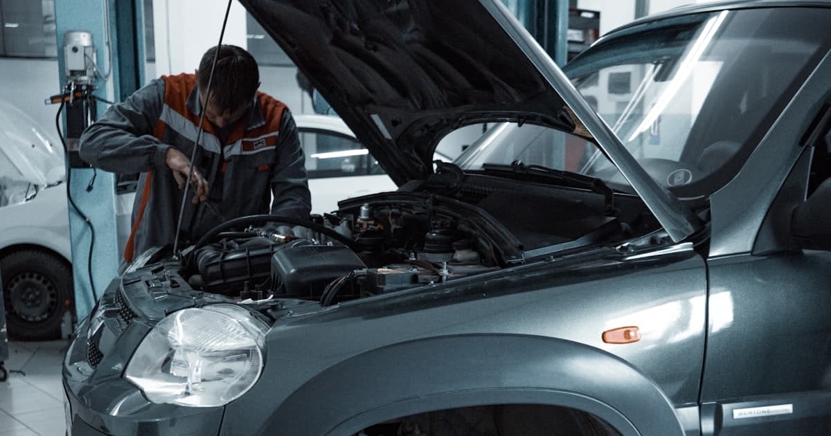 Mechaniker arbeitet in der Werkstatt eines Autohauses an einem Fahrzeug mit offener Motorhaube